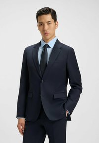 Abito blu navy con vestibilità sartoriale, design a un petto, rever a notched, chiusura a due bottoni, abbinato a una camicia azzurro chiaro e una cravatta testurizzata.