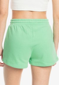 Shorts en coton verts avec une taille élastique, présentant une texture lisse et un ourlet arrondi. Coutures visibles et sans poches.