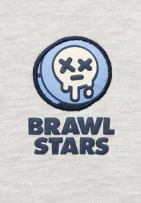 Šedá textília s vyšívanou kruhovou nášivkou so vzorom lebky a textom "BRAWL STARS" v tmavo modrom, textúrovanom písme.