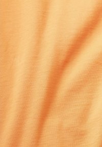 Tissu doux et léger de couleur orange uni, offrant une texture lisse avec de légers plis, adapté aux vêtements décontractés ou au superposition.