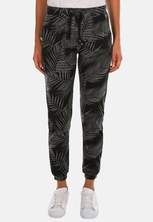 Schwarze Jogginghosen mit einem grauen Palmblätterdruck, mit einem elastischen Bund und Kordelzug sowie schmal zulaufenden Bündchen. Getragen mit weißen Sneakers.