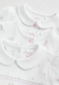 To babybeklædningsgenstande i hvidt stof, med bølgede kraver, knaplukninger og et blomsterprint med kaniner i bløde lyserøde nuancer.