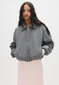 Grå bomberjakke i uldblanding med lynlås, krave og elastiske manchetter, med sidelommer og en struktureret overflade.