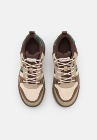 Sportskor med en överdel i beige och brun mocka med gröna detaljer, runda snörning, och en vadderad sula. Toppvy.