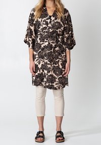 Svart blommig kimono med vida ärmar, tillverkad av lätt material, med ett bälte i midjan, bärs över ljusbeige cropped-byxor och svarta sandaler.