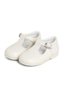 Zapatos de cuero sintético blancos con punta redonda, diseño de tira en T y hebilla ajustable. Textura suave con detalles perforados en el interior.