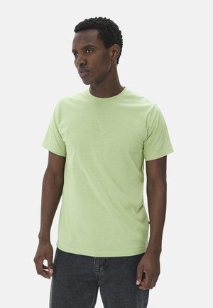 Camiseta corta de manga corta en un suave tejido texturizado de color verde claro. Cuello redondo con un corte relajado. Modelo combinada con jeans oscuros.