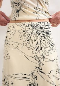 Gros plan d'une personne ajustant une jupe beige et un haut avec un imprimé floral en lignes noires, montrant le ventre et les mains tirant sur le tissu.