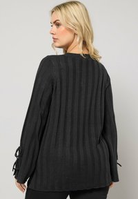 Czarny sweter w paski o luźnym kroju, wykonany z teksturowanej dzianiny z zapięciami na wiązanie przy rękawach. Posiada okrągły dekolt i ściśnięty materiał.