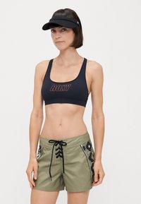 Soutien-gorge de sport noir avec le logo "ROXY", associé à un short vert olive avec un devant à lacets et des panneaux latéraux à motifs. Détails d'accent en noir.