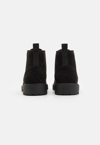 Stivaletti neri in suede con suola in gomma nera spessa, dotati di una linguetta sul retro e design arrotondato per una facile vestibilità.
