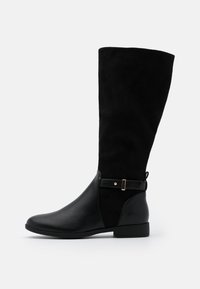 Bottes noires montantes en cuir et daim, dotées d'une semelle plate, d'un bout arrondi et d'une sangle décorative avec un accent doré.
