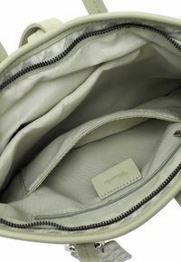 Intérieur de sac à main vert présentant un compartiment zippé, une doublure en tissu lisse et un patch avec logo. Contient plusieurs poches pour l'organisation.