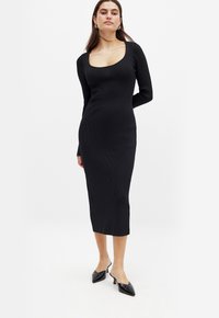 Czarna sukienka w prążki z długimi rękawami, okrągłym dekoltem i długością midi. Para czarnych, eleganckich klapek na obcasie dopełnia stylizację. Miękka tekstura.