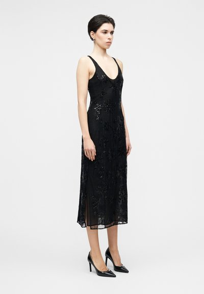 Robe de soirée noire avec un décolleté en V profond, ornée de paillettes et de motifs floraux, présentant une coupe longueur genou avec des fentes latérales.