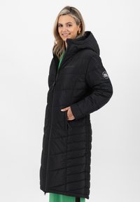 Cappotto invernale imbottito nero con cappuccio, dotato di cerniera frontale, tasche laterali e cuciture decorative. Il tessuto sembra liscio e leggero.