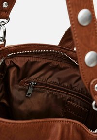 Interieur einer braunen Lederhandtasche mit glatter Textur, ausgestattet mit einer Reißverschlusstasche und einem Logopatch. Akzente setzen silberne Beschläge.