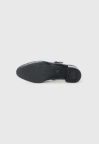 Semelle d’une chaussure habillée en cuir noir avec une semelle en caoutchouc texturée et un petit talon, marquée « Tamaris » et « ANTISTON ».
