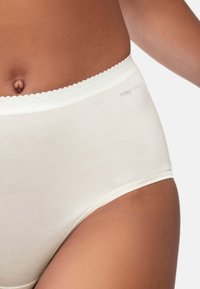 Slip a vita alta, color crema, realizzato in tessuto morbido, con un bordo scallop e un logo discreto sull'elastico in vita.
