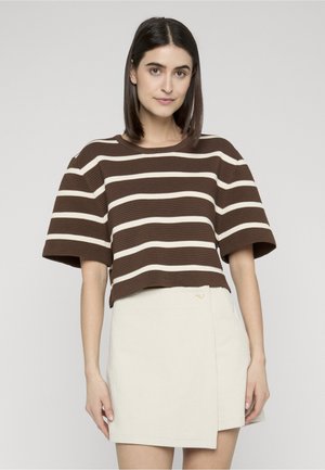 Woman with straight dark hair wearing a brown and white striped short-sleeve top and a cream-colored mini skirt with a side button.