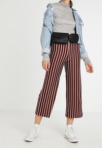 Veste en jean bleu clair sur un col roulé gris, associée à un pantalon culotte rayé bordeaux et blanc et des baskets blanches montantes. Sac banane noir inclus.