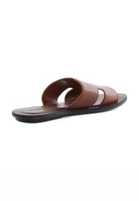 Brown leather slide sandal with open toe and sides, textured upper, and a flat black sole. Minimalist design featuring two cut-out sections.