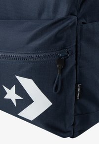 Námornícka modrá batoh s textúrovanou tkaninou, so zipsom, bielymi hviezdami a logom chevron a s označením značky na boku.