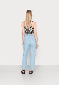 Black and white marbled crop top with thin straps paired with light blue, loose-fit trousers and black flat sandals, viewed from the back.