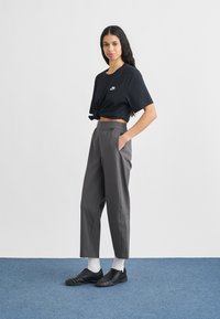 Fekete rövidített póló fehér logóval, szürke magasderekú nadrág, fekete sportcipő fehér zoknival, kék padlón.