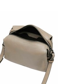 Borsa a spalla in pelle beige con chiusura a zip, interno visibile, tracolla regolabile e texture liscia. Presenta un branding minimale.
