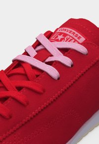 Κόκκινο αθλητικό παπούτσι Converse με κορδόνια σε ανάμεικτο κόκκινο και ροζ χρώμα, που δείχνει την ετικέτα στη γλώσσα με τη σήμανση Converse All Star.