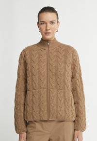Veste zippée en tricot torsadé marron avec un col haut, présentant un motif texturé et une coupe décontractée. Tissu doux avec des poignets côtelés.
