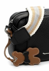 Borsa in pelle nera strutturata con tracolla intrecciata in beige, grigio e bianco. Presenta un charm a forma di orsacchiotto marrone con dettagli neri.