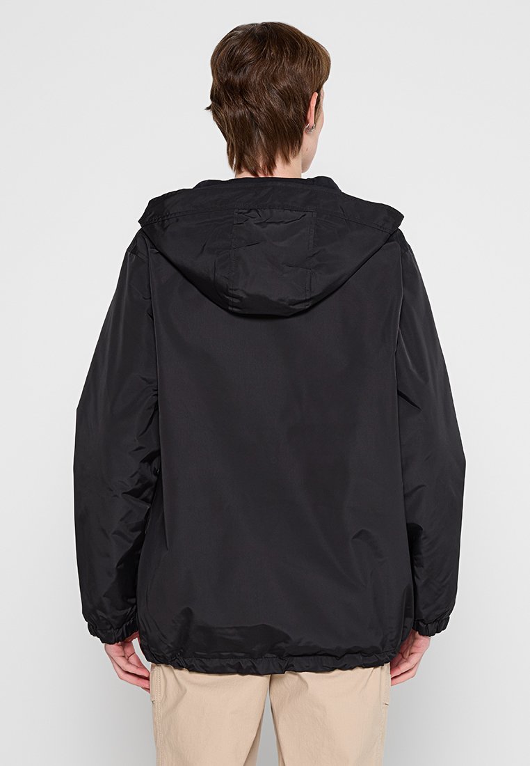 Schwarze Kapuzenjacke mit elastischen Bündchen und Saum, aus einem glatten, wasserabweisenden Material hergestellt, mit einem einfachen, minimalistischen Design.
