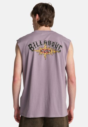 Uomo che indossa una maglia viola senza maniche con la scritta "Billabong" e una grafica del sole sul retro, in piedi davanti a uno sfondo semplice.