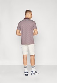 Kortärmad polo t-shirt i ett vinrött mönster, matchad med ljusa shorts. Har en krage, subtil struktur och sportskor.