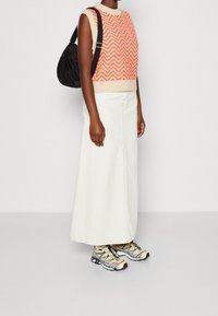 Strikket ærmeløs sweater i orange og creme zigzag mønster, båret med en hvid denim maxi nederdel og kraftige sneakers med multicolor accenter.