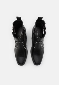 Black ankle boots made of textured leather, featuring silver studs, a side zipper, and a pointed toe design.