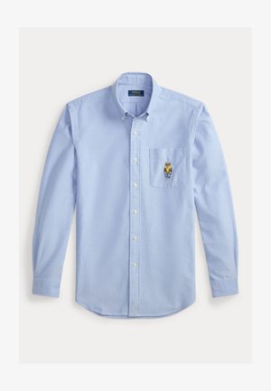 Svetlo modra srajca z dolgimi rokavi iz bombaža, z žepom na prsih in vezanim dizajnom medveda. Dolgi rokavi z gumbastimi manšetami.