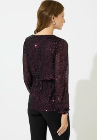 Paarse pailletten top met lange mouwen en een getailleerde taille, met een ronde halslijn en glanzende textuur, gecombineerd met zwarte, strakke broek.