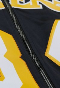 Schwarz-gelbe Sportbekleidung mit einem auffälligen Reißverschluss, ausgestattet mit fettem Text und kontrastierenden Zickzackmustern in Gelb und Weiß. Weicher Stoff.