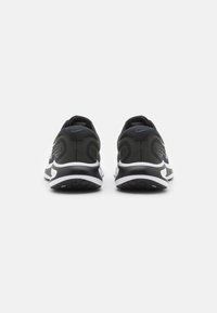 Un paio di scarpe da corsa nere e bianche viste da dietro su uno sfondo bianco semplice, con sottili motivi scuri e logo Nike.