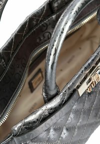 Borsa a tracolla trapuntata argento metallizzato con texture a motivo, manici doppi e aperture della cerniera visibile che mostra l'interno beige.