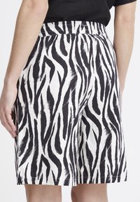 Shorts à imprimé zèbre noir et blanc avec une taille élastique, présentant une coupe décontractée et un ourlet au genou. Tissu en coton avec une finition texturée.