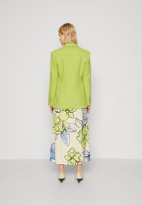 Limoengroene gestructureerde blazer met een tailored fit, gecombineerd met een crèmekleurige maxi rok met bloemenprint met blauwe en groene accenten.