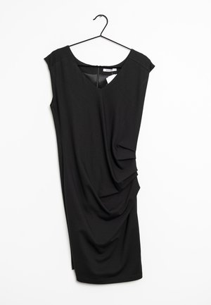 Vestido negro sin mangas con escote en V y detalles drapeados en el costado. Hecho de una tela suave, cuelga de una percha negra sobre un fondo blanco.