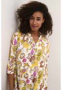 Abito stampato bianco, caratterizzato da motivi floreali e a ricciolo in giallo, rosa e viola. Con colletto, maniche a tre quarti e vita arricciata.
