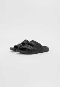 Tongs noires en caoutchouc avec trois sangles courbes et une semelle texturée pour une meilleure adhérence. Présentent un design léger et facile à enfiler.