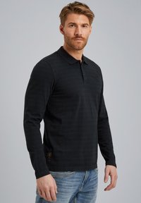 Camisa polo de manga larga negra con finas franjas horizontales, color y una tapeta con botones; material de algodón con una textura suave.