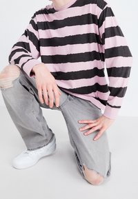 Maglietta a maniche lunghe con righe irregolari rosa e nere, abbinata a jeans grigi strappati e sneakers bianche.